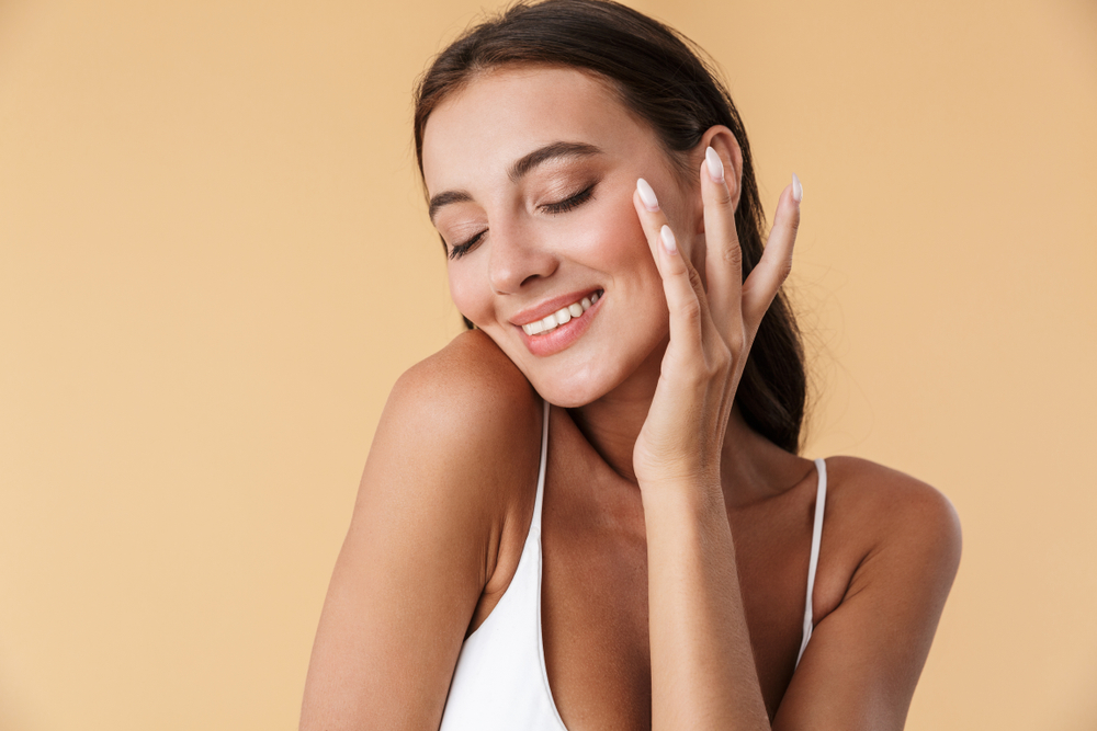 Young woman smiling, touching her smooth, clear skin after Fraxel laser treatment for acne scars.