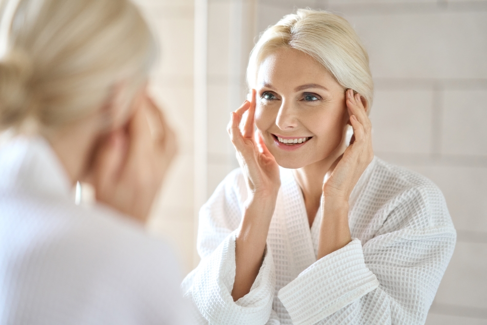 Senior woman admiring her rejuvenated, tighter skin in the mirror after a non-surgical Ultherapy treatment.